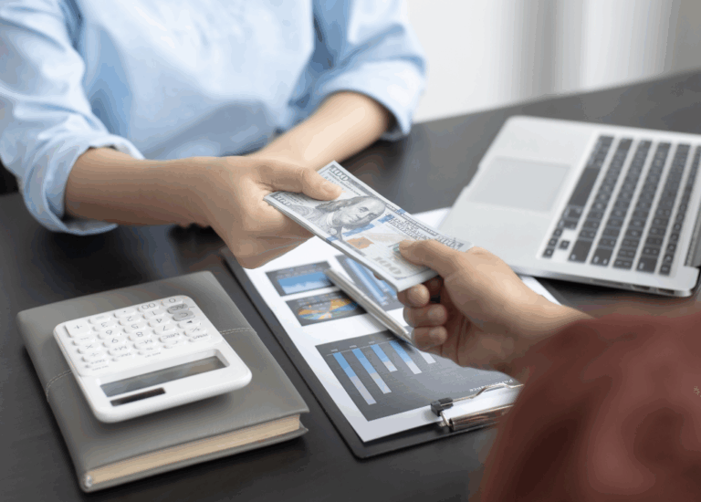 Przekazanie gotówki nad dokumentami finansowymi i laptopem – symbolizujące windykację należności i sprawy o zapłatę.