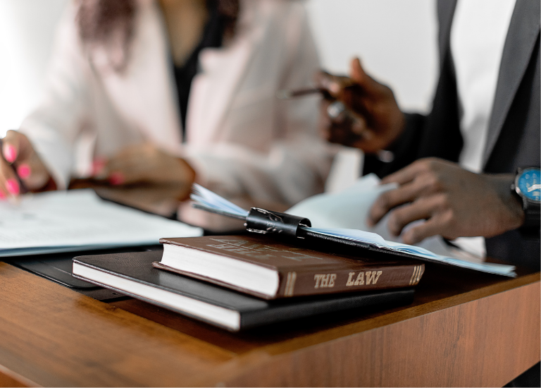 Dwóch prawników analizujących dokumenty przy biurku z książką „The Law” – symbolizujące sprawy cywilne i doradztwo prawne.